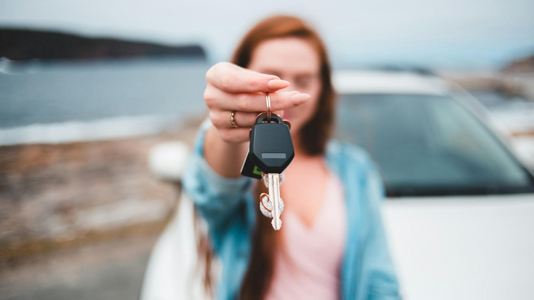 Une femme tend des clefs de voiture. La voiture est derrière elle. Les clefs sont nettes, tout l'arrière plan est flou.